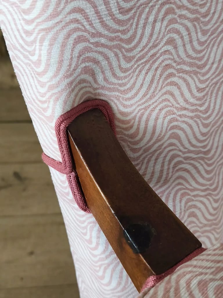 Détail d&rsquo;un tissu ondulé rose et de son passepoil, sur le bois d&rsquo;un fauteuil