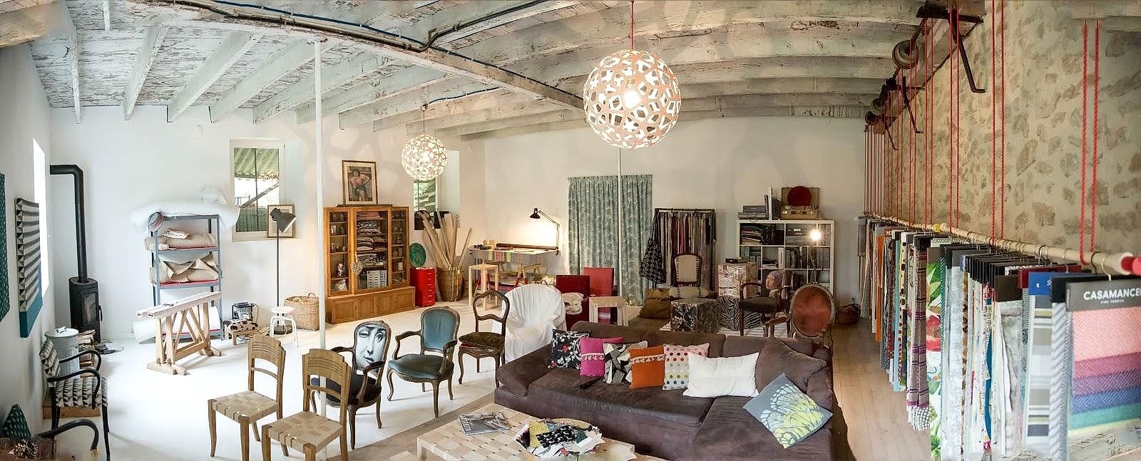 L&rsquo;atelier et le show-room installés dans une ancienne magnanerie&nbsp;: poutres blanchies, mur de pierre et rouleaux de tissus suspendus